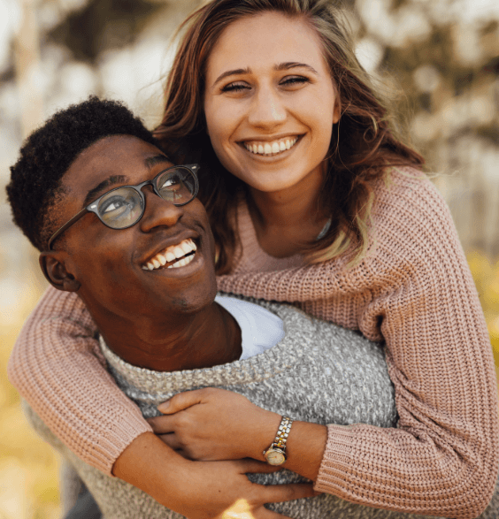 A young man and woman smile and laugh together, showcasing their bright, healthy teeth in a dental setting.