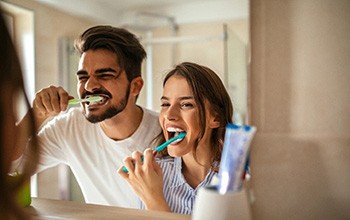 a couple brushing their teeth while looking in a bathroom mirror