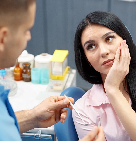 Woman in dental chair holding her cheek in pain due to dental implant failure in Roslyn